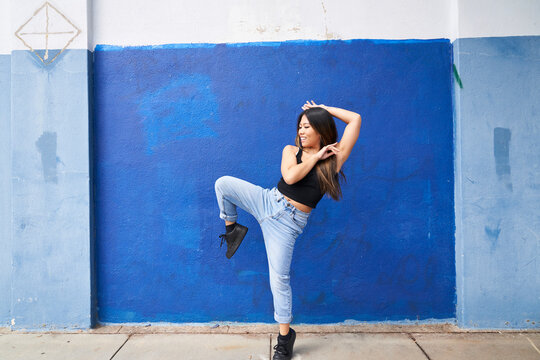 Woman dancing in front of blue wall outdoors kicking