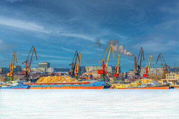 Fototapeta premium Barges, cranes, ships for the transport of heavy goods, iron ore, sand in the river cargo port in winter. Industrial landscape.