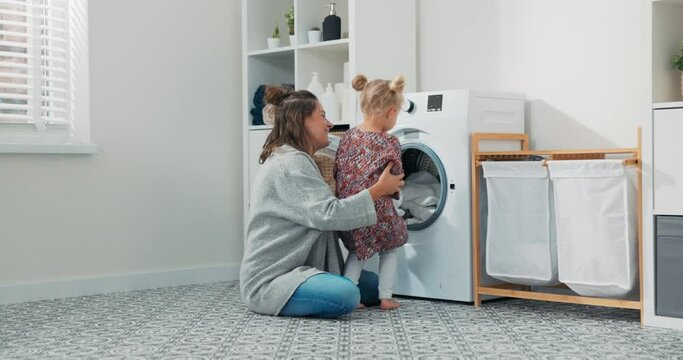 Woman spends time with young child in laundry room, bathroom, performs household duties while on maternity leave, takes care of daughter, shows girl how to operate washing machine.