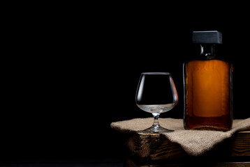 Empty glass of whiskey and bottle of whiskey on black background. Copy space