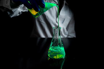A woman scientist experimenting with a yellow fluorescent solution in a glass conical flask in dark...