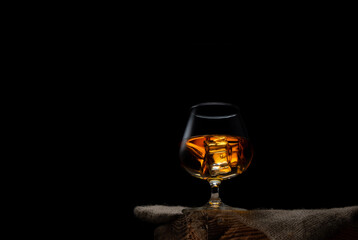 a glass of whisky with ice cubes on black background
