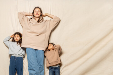 Little sisters and an attractive young mother have fun on a beige background in jeans and sweatshirts, spending time together at home. Women's generation. International Women's Day. mother's day.