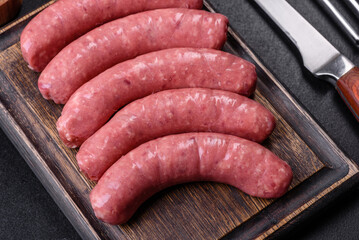 Raw sausages with ingredients on a cutting board on a stone background with copy space