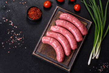 Raw sausages with ingredients on a cutting board on a stone background with copy space © chernikovatv