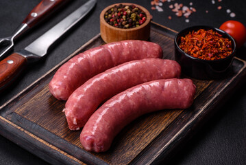 Raw sausages with ingredients on a cutting board on a stone background with copy space