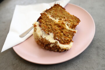 A close-up of a delicious slice of carrot cake on a soft, pink plate.