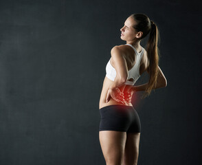 Thats painful. Studio shot of a sporty young woman holding her lower back in pain against a dark...