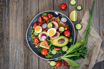 Appetizing vegetable salad with eggs, avocado on a wooden background.