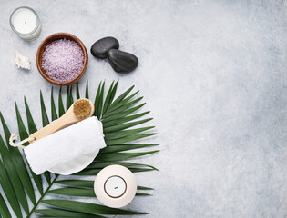 Fototapeta na wymiar Creative flat lay of facial and body care cosmetics for spa with sea salt, massage stones, candles, towel, brush and palm leaf on blue background. Top view and copy space