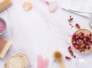 flat lay with organic sea salt with dried rose flowers, soap, candle, brush and gua sha on a pink marble background in frame. The concept of a natural spa product. Top view and copy space