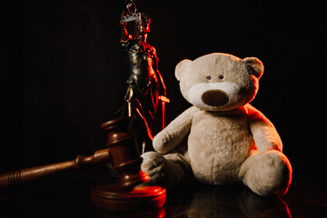 Judge gavel, figure of lady of justice and teddy bear in a dark court room. Law and children concept