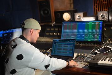 Young music producer working in sound recording studio. Sound engineer sitting at laptop and mixing...