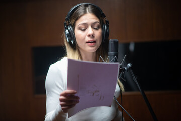 Portrait of young female performer recording song in studio. Caucasian woman holding text and singing song on radio or at sound recording studio. Creating music concept