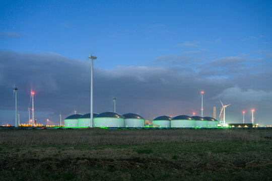 Netherlands, Eemshaven, Wind turbines and storage tanks at dusk