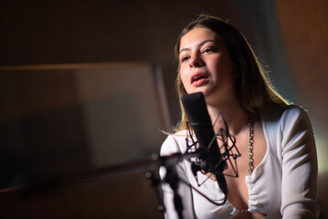 Portrait of woman recording song in sound production studio. Young Caucasian female performer singing at live concert. Creating music concept