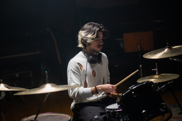 Concentrated young man training on drum set in studio. Musician with headphones rehearsing or...
