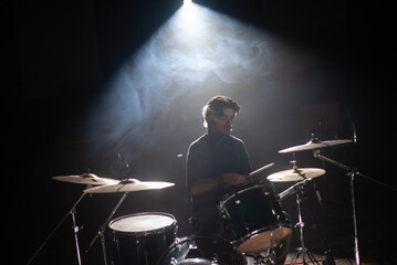 Concentrated young drummer training in dark hall with smoke in background. Rock musician rehearsing...