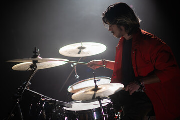 Concentrated young man playing drum set at concert. Portrait of musician performing on drum set or...