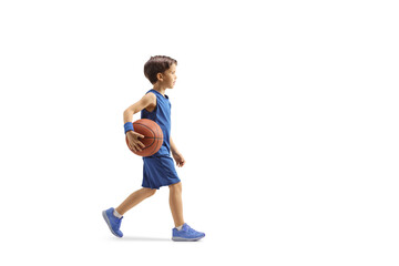 Full length profile shot of a boy in a blue jersey walking and holding a basketball