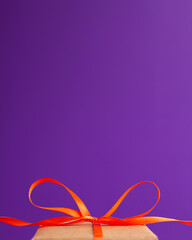 Close up of an orange satin ribbon bow at the bottom on vibrant purple blurred background with copy space. Holiday presents and Halloween concept