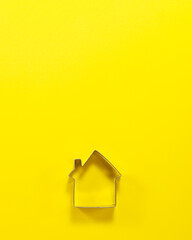 Steel house shaped cutter for cookies from above. Flat lay top view. Confectionery cooking concept with copy space on bright yellow paper background.