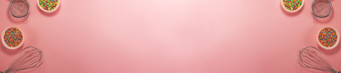 Banner of cupcake liners with colored sugar inside whisk and strainer flat lay top view. Confectionery cooking concept with copy space on bright pink paper National cooking day