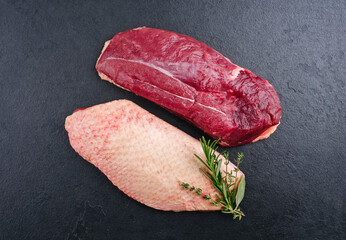 Traditional raw gourmet duck breast filet with skin offered with herbs as top view on a black board