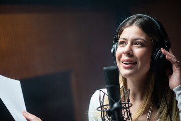 Young happy female singer or radio host working in studio. Portrait of Caucasian woman sitting in headphones at microphone. Creating music concept