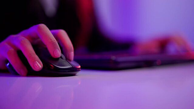 Close-up hand and mouse playing games. Young woman sitting on chair with computer pc. Happy female Professional Streamer playing game online in dark room neon light.