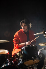 Concentrated young man playing drum set in garage. Portrait of musician training playing drums or recording in studio. Drummer training concept