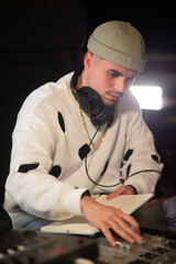 Portrait of concentrated young dj at mixing console panel. Caucasian music producer wearing cap and...