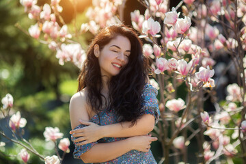 Fototapeta premium Beautiful girl with flowers of magnolia. Portrait of young smiling brunette woman under blossom magnolia tree.