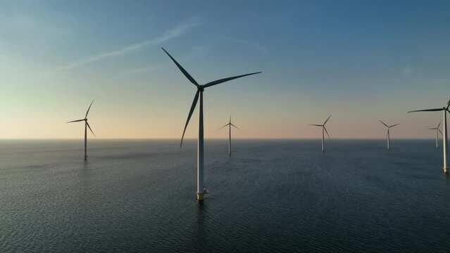 Wind turbines producing sustainable renewable energy in an offshore wind park during sunset. 