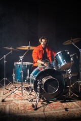 Young Caucasian man sitting at drum set in studio. Rock musician training or rehearsing in garage....