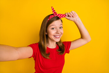 Portrait of adorable sweet cheerful little girl take selfie video blog influencer adjust headband isolated on yellow color background