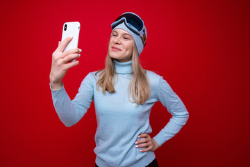 Naklejka premium Portrait of a young woman in a sweater and ski goggles with a phone