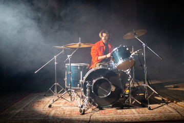 Portrait of young man playing drum set in studio with smoke in background. Musician sitting in...