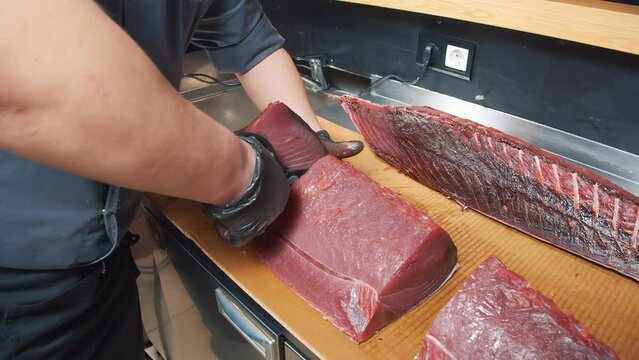 Close-up of the process of cutting tuna fish at the market. Male hands in gloves cutting a large fish with a knife.