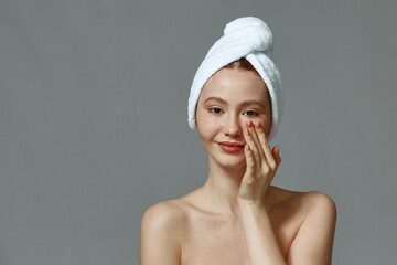Young girl with bare shoulders, towel on head apply cream on healthy smooth skin, massage face....