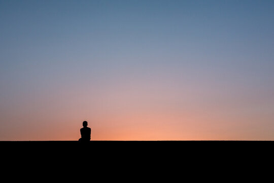 Junge sitzt auf Mauer nach Sonnenuntergang
