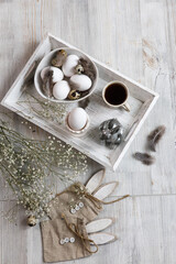 Fototapeta na wymiar Table decorated for Easter in beige tones. Dried gypsophila, chicken and quail eggs, a silver figurine of a hare and a cup of coffee. Easter concept.