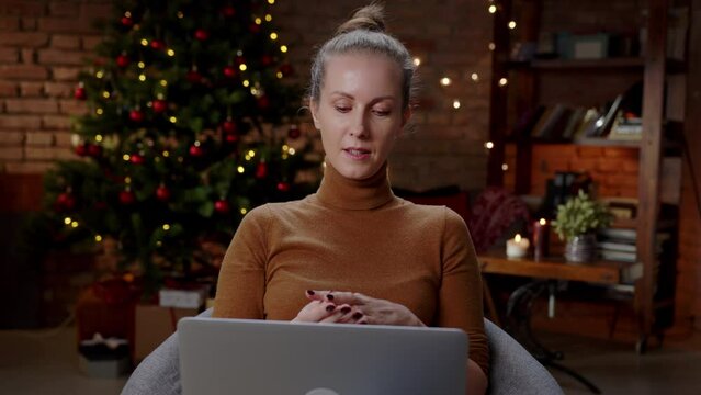 Woman working from home in home office at Christmas. Cozy dark living room in Winter.