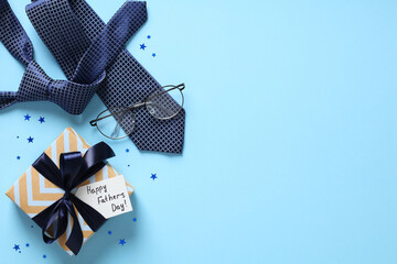 Flat lay composition with Fathers Day gift, necktie, eyeglasses, confetti on pastel blue background.
