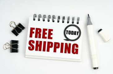 On a white surface lies a marker, clips and a notebook with the inscriptions Today and FREE SHIPPING