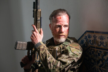Fototapeta premium Attentive army man during battle. Caucasian man with beard with smears of blood on face holding machinegun. Military, army, danger, fighting, airsoft concept