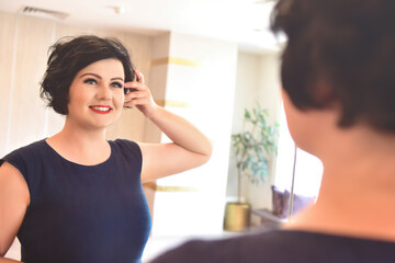 Happy Morning. An attractive young full body woman looks at herself in the mirror in her apartment.