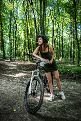 Fototapeta premium Young sexy woman wear green short dress rides a bicycle in the forest, spend time on summer day