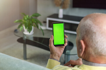 Bald elderly man holds smart phone with empty green screen for mockup