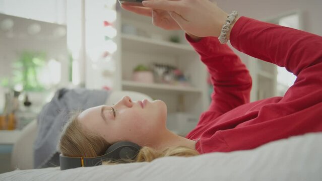 Teenage girl wearing wireless headphones streaming music or film from mobile phone  -s hot in slow motion